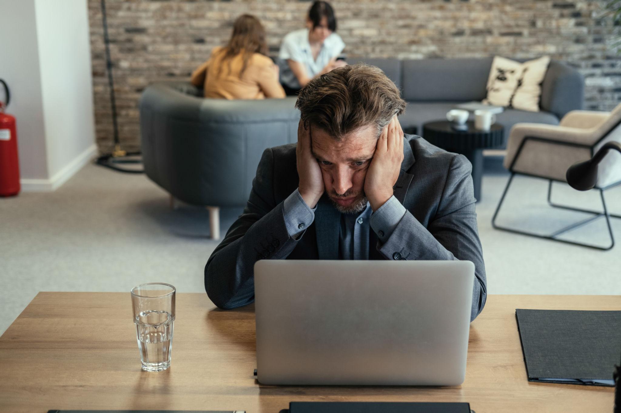 A distressed business professional at a laptop seeking help with a difficult problem